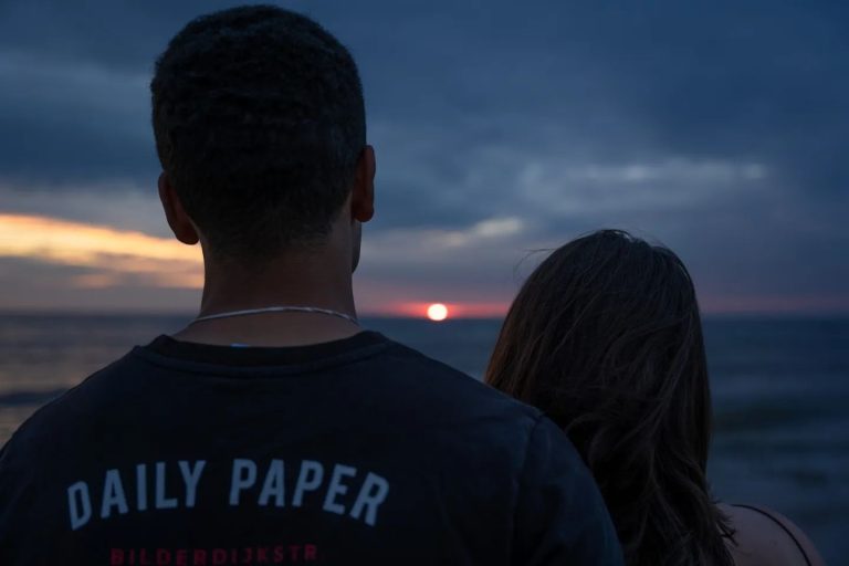 Koppel van achteren uitkijkend over zee bij zonsondergang