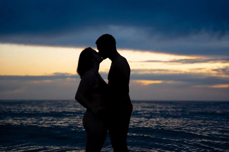 Silhouet van een kussend koppel op het strand bij schemering