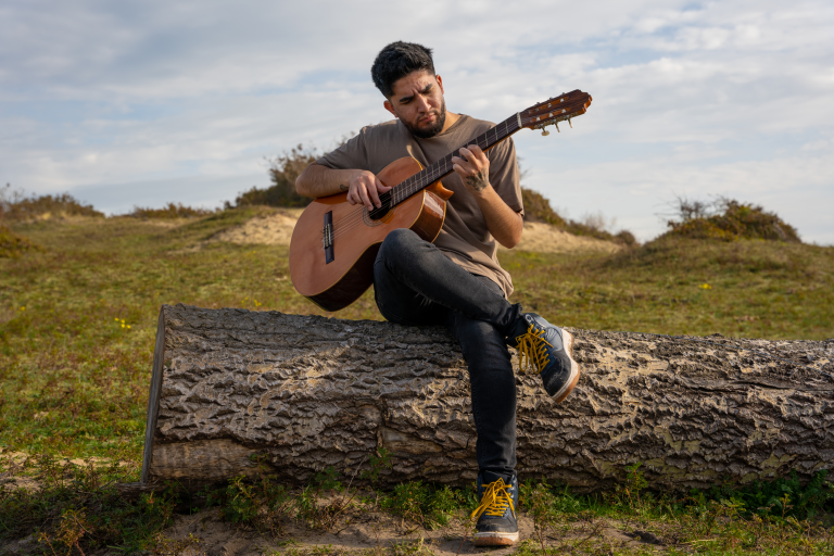 Man speelt akoestische gitaar op een boomstam buiten