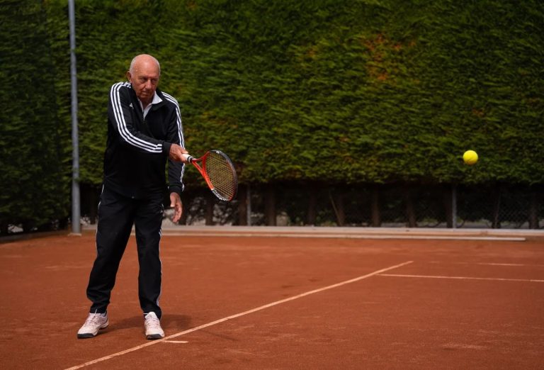 Oudere man slaat een tennisbal op een buitenbaan